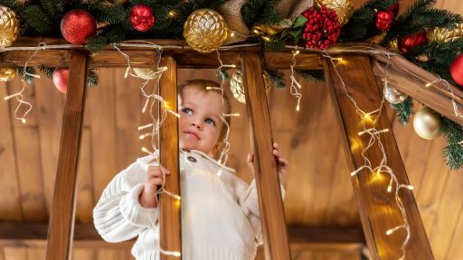 Kind steht am Geländer mit Weihnachtsschmuck und Lichterkette, Foto: Colourbox