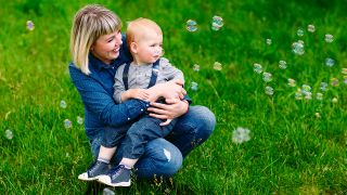 Frau mit Kind auf dem Arm gucken Seifenblasen hinterher, Foto: Colourbox