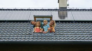 Familie guckt aus einem Dachfenster. Auf dem Dach befindet sich eine Solaranlage, Foto: Colourbox