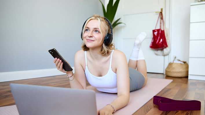 Junge Frau mit Kopfhörern auf Sportmatte, Bild: IMAGO/Zoonar.com/Phongthorn Hira Junge Frau mit Kopfhörern auf Sportmatte, Bild: IMAGO/Zoonar.com/Phongthorn Hira