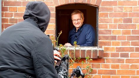 Luzyca-Moderator Christian Matthée schaut aus einem Backstein-Haus und wird dabei von einem Kameramann gefilmt.